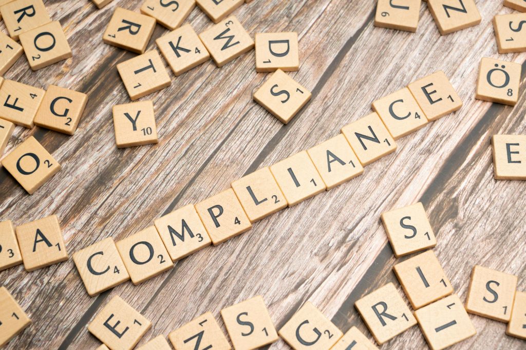 Corporate Compliance Wooden letter tiles forming the word 'COMPLIANCE' on a rustic wooden background.