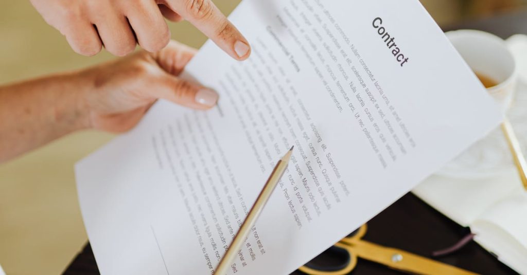 Employment Matters Hands pointing at contract on desk with laptop, indicating collaboration