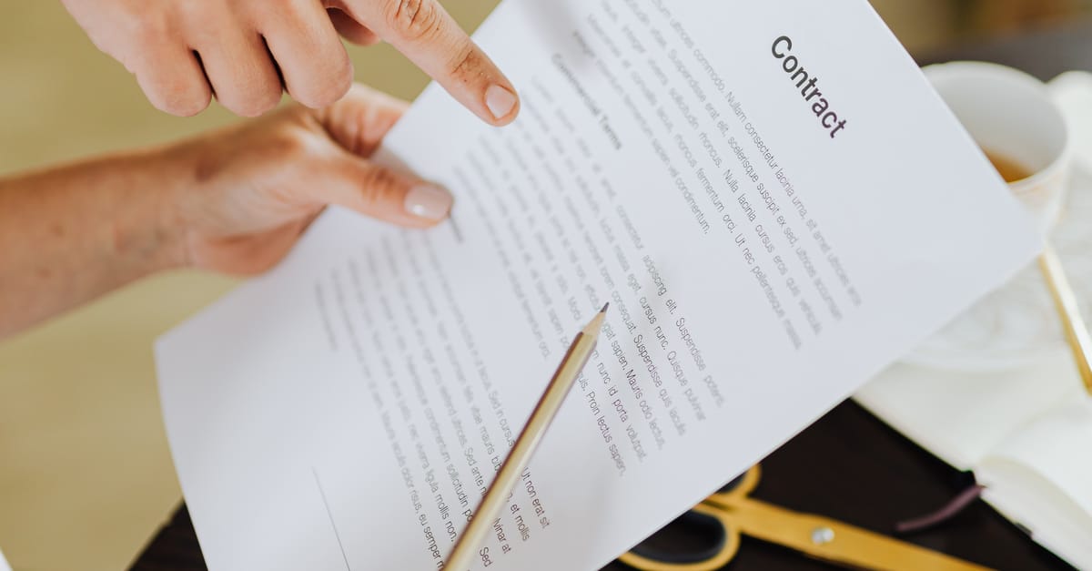 Hands pointing at contract on desk with laptop, indicating collaboration